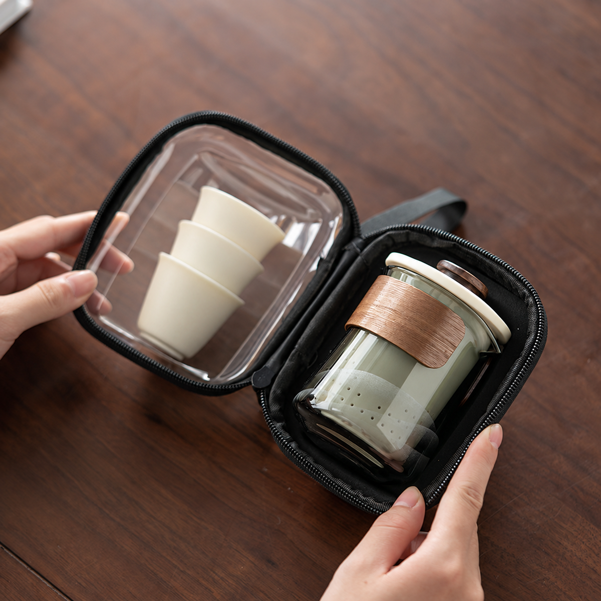 Hands opening the clear-front zip case to show the brewer and three nested ivory cups