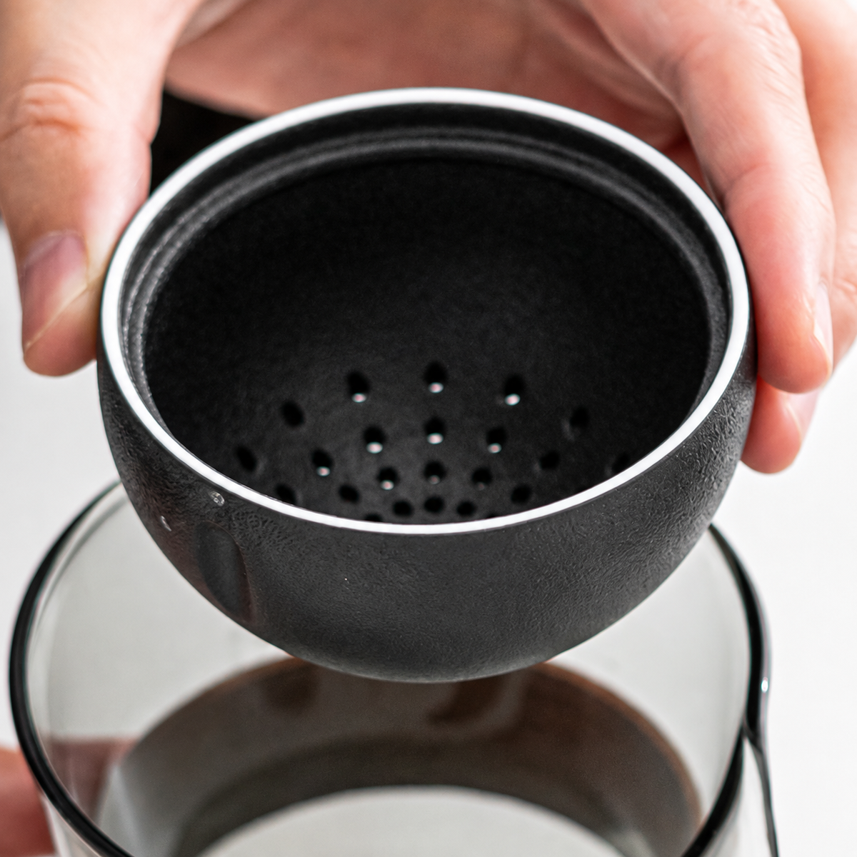 Close view of the black ceramic infuser and its perforated base above the glass brewer