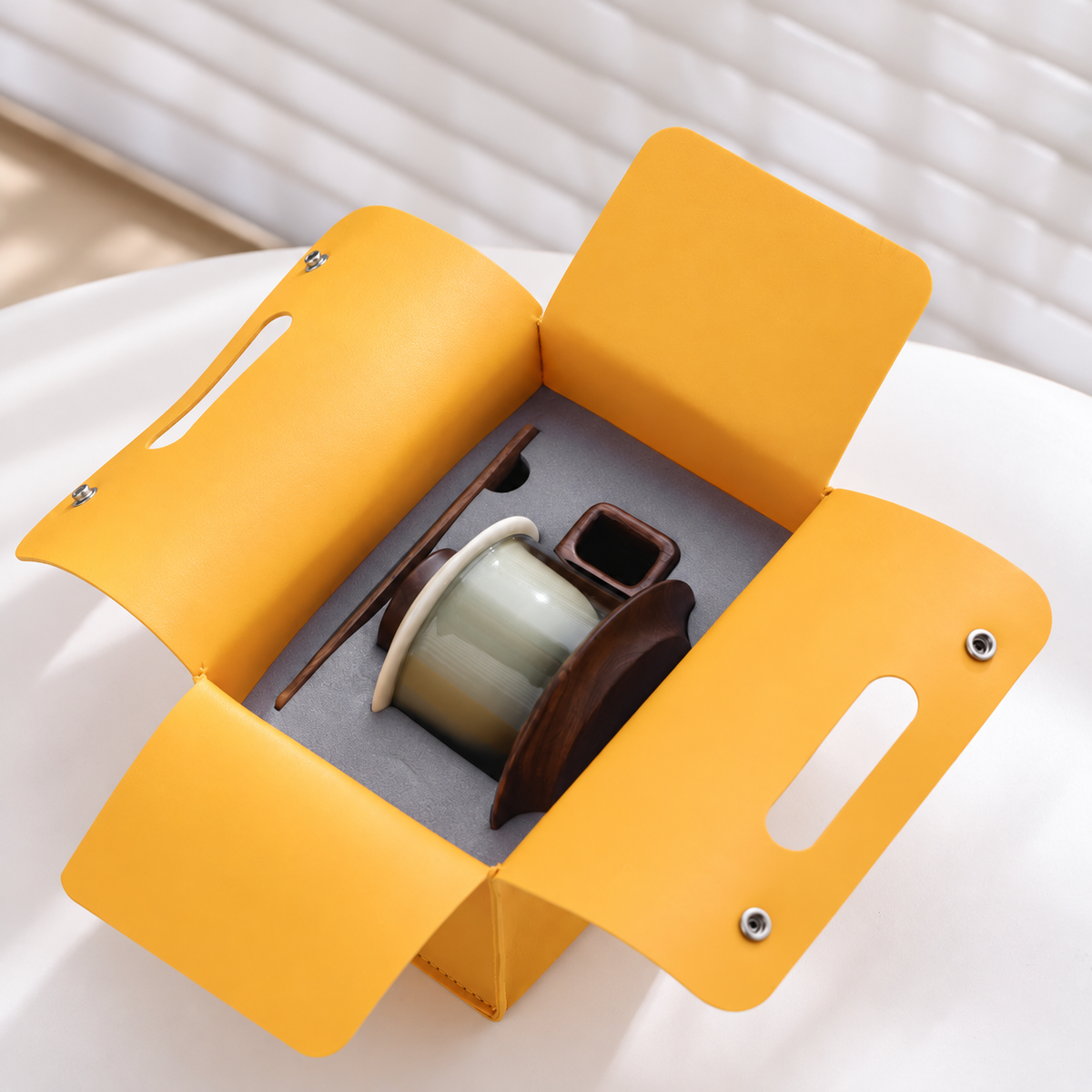 Open yellow presentation case with fitted interior holding the glass mug, saucer and wooden stirrer