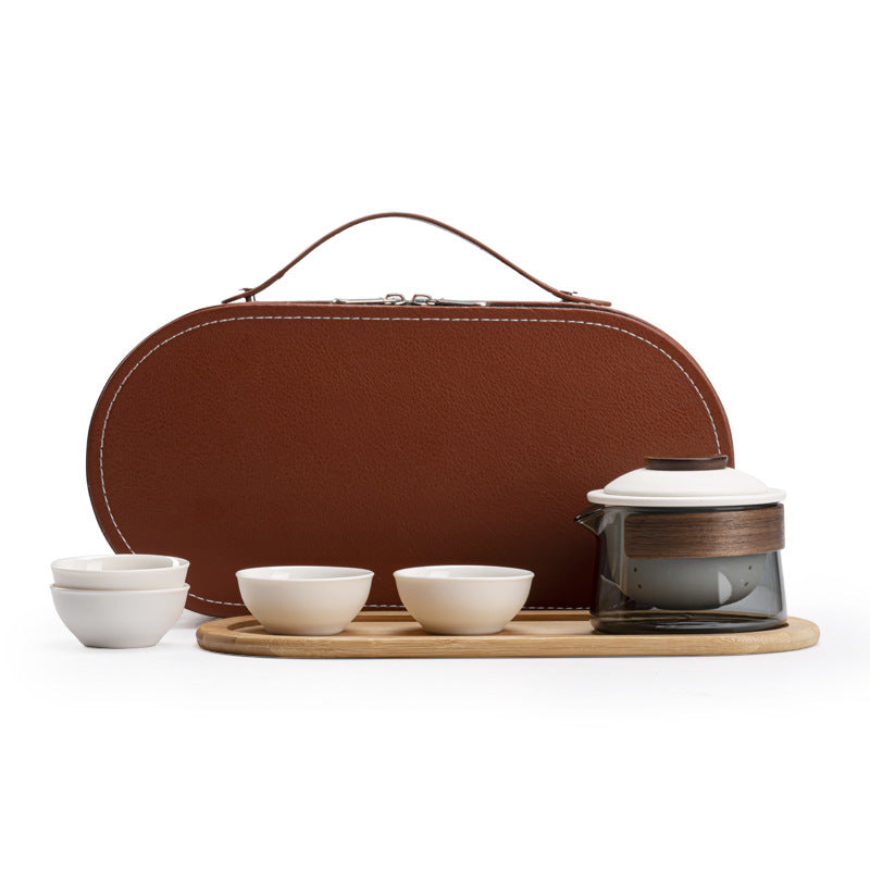 Glass tea brewer with wood grip, four white cups, bamboo tray and closed brown carrying case