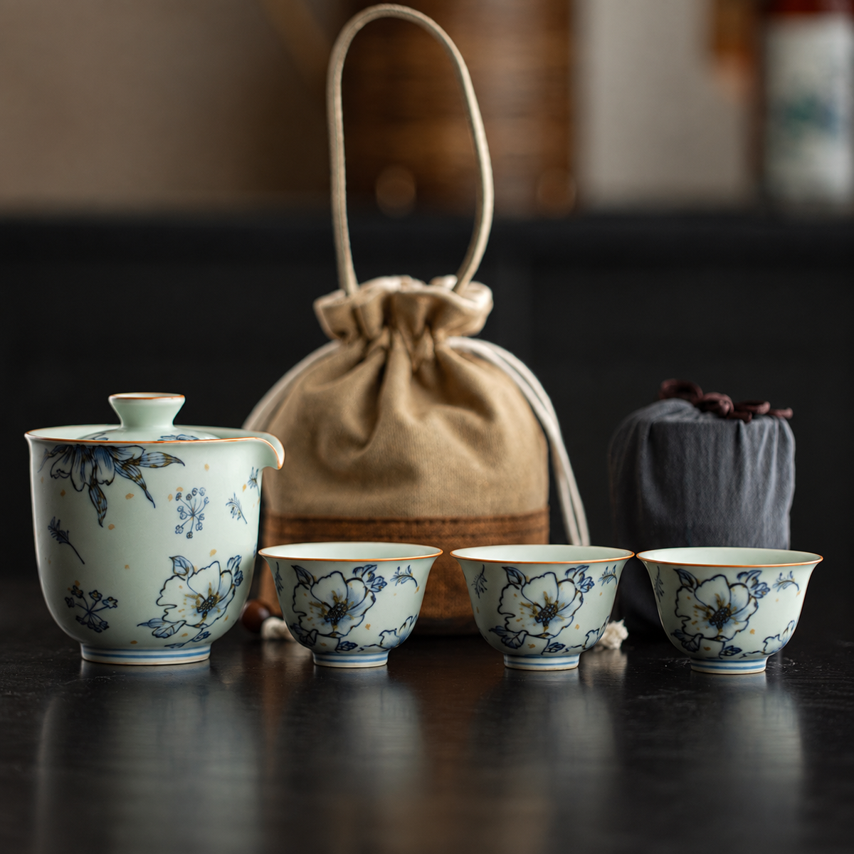 Blue floral painting on a celadon brewer and three cups with tan carrying bag and dark pouch