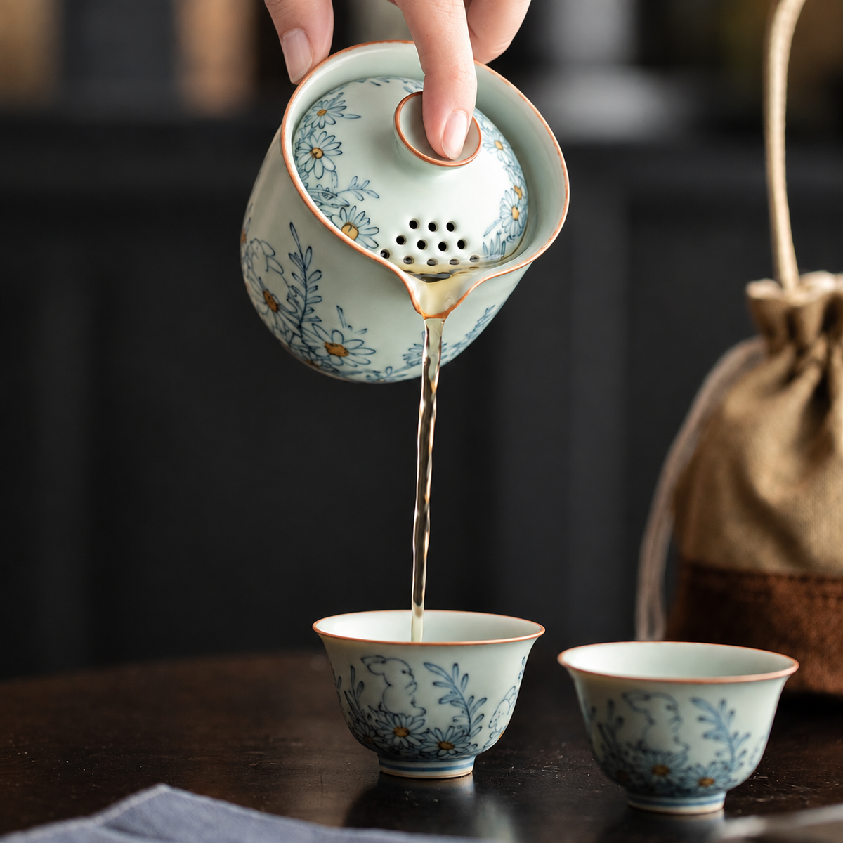 Fingertips tilting the rabbit-pattern brewer to pour tea through the perforated lid into a matching cup