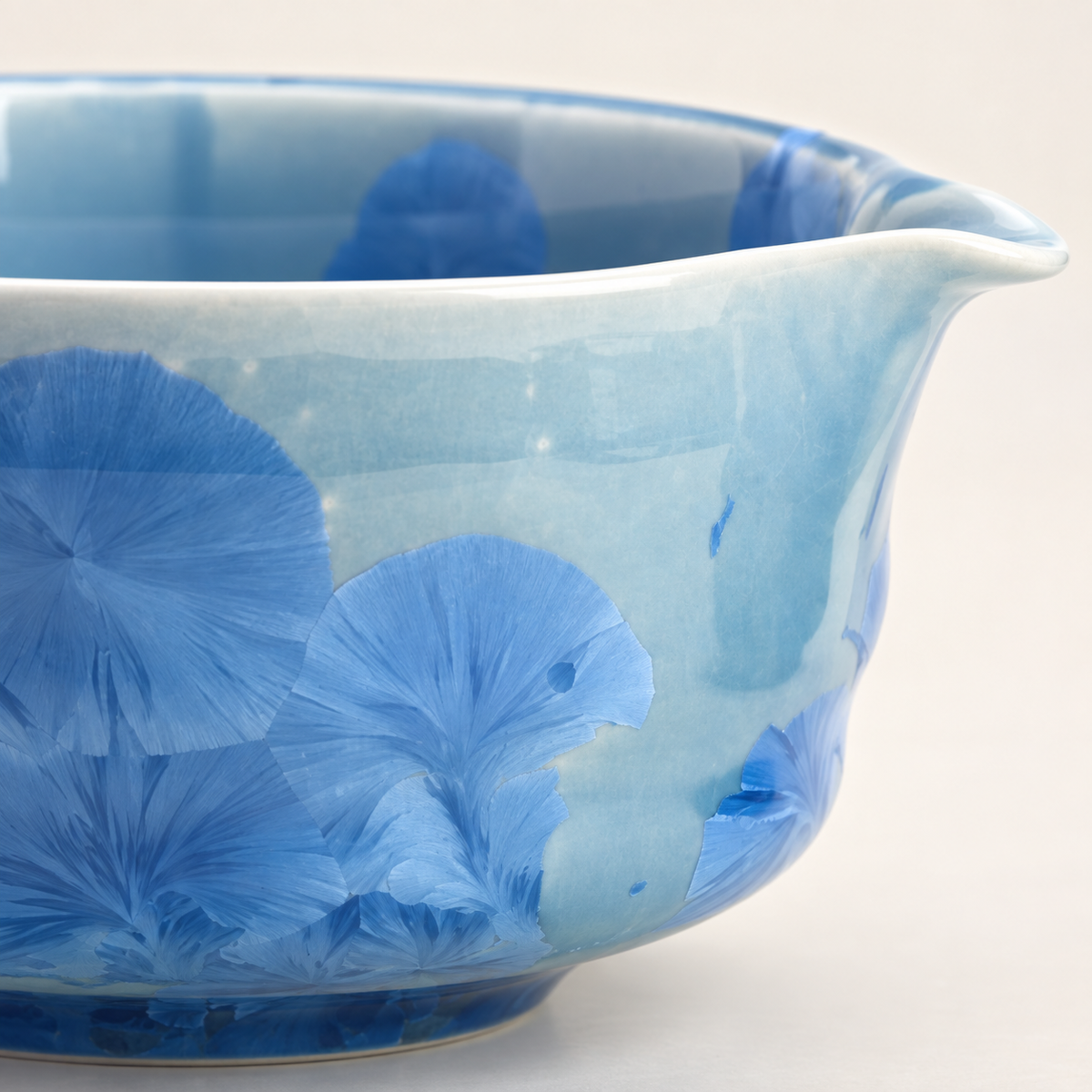 Close view of blue crystalline glaze blooms, the bowl rim and its formed pouring spout
