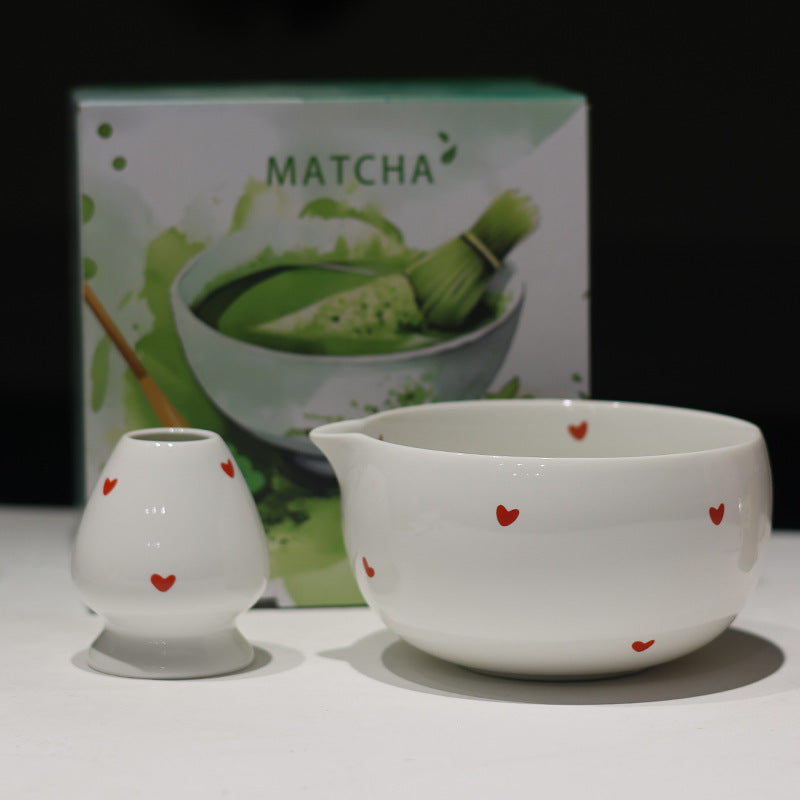 White ceramic matcha bowl and whisk holder with red hearts, shown with the retail box